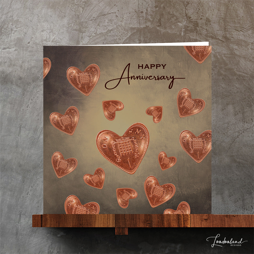 Greeting card with heart-shaped copper coins and 'Happy Anniversary' text on a textured surface.