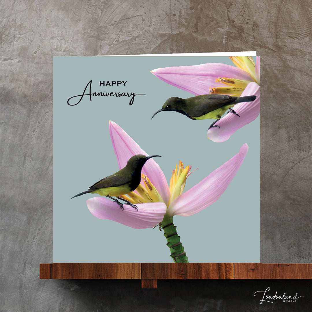 Designer Anniversary greeting card with birds on pink tropical flowers and 'Happy Anniversary' text on a pale blue background