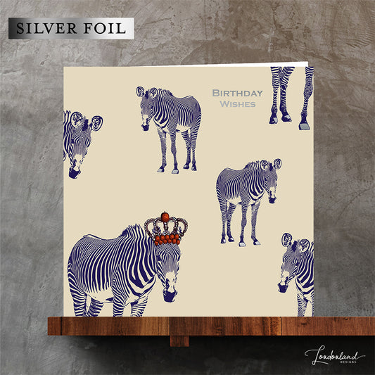 Designer birthday card of zebras with blue stripes wearing a crown of red apples. Wording and zebra hooves are designed using silver foil for a luxury finish. 