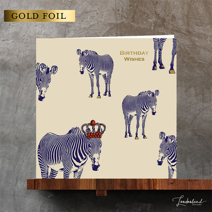 Designer birthday card of zebras with blue stripes wearing a crown of red apples. Wording and zebra hooves are designed using gold foil for a luxury 