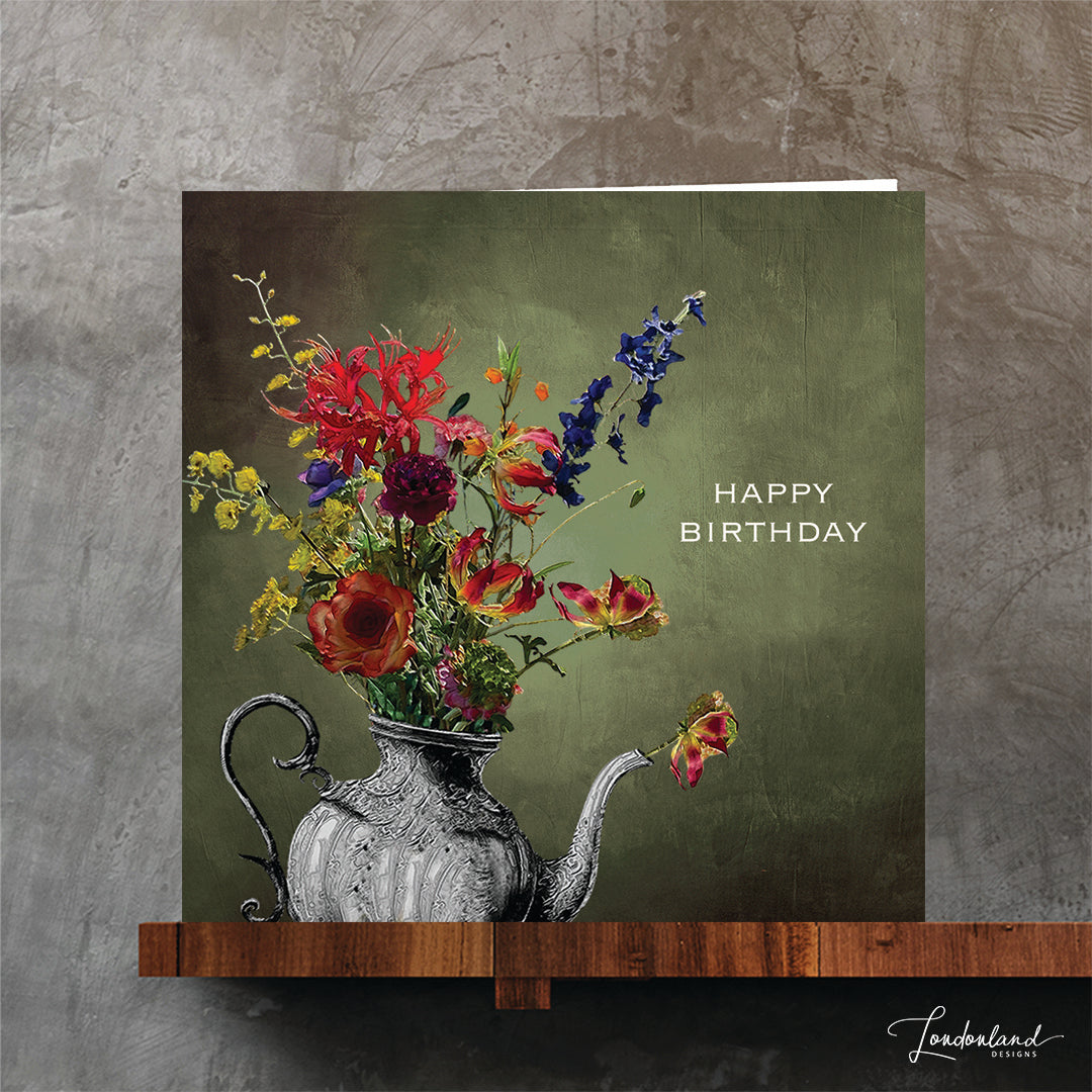 Silver teapot vase holding a bunch of flowers and 'Happy Birthday' text on a green background. Designer birthday card.