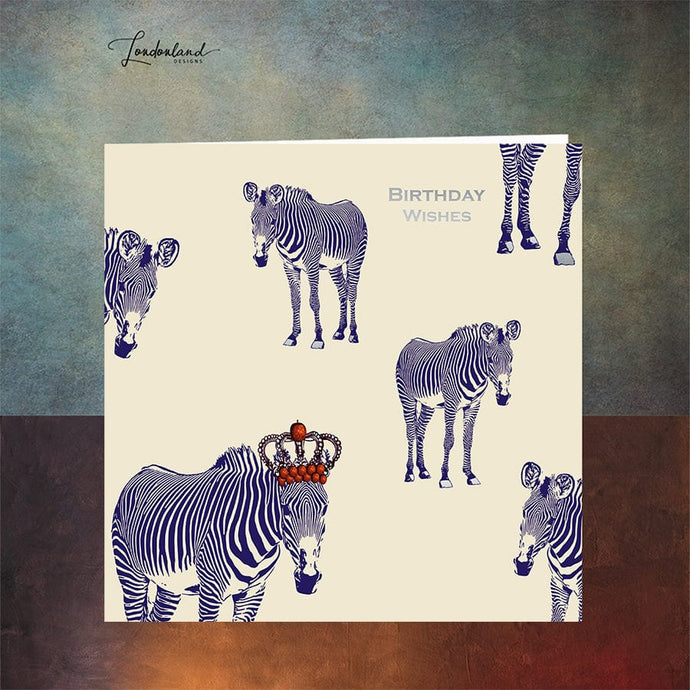 Designer birthday card of zebras with blue stripes wearing a crown of red apples. Wording and zebra hooves are designed using silver foil for a luxury finish. 