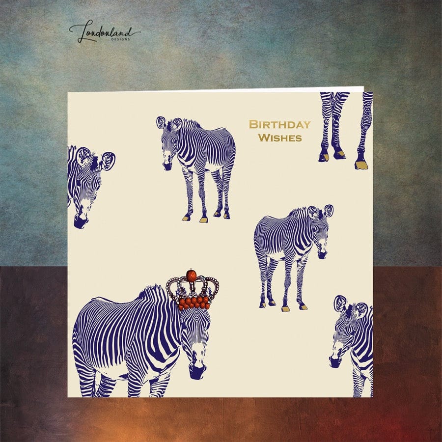 Designer birthday card of zebras with blue stripes wearing a crown of red apples. Wording and zebra hooves are designed using gold foil for a luxury finish. 