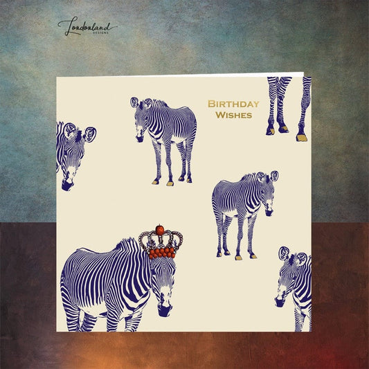 Designer birthday card of zebras with blue stripes wearing a crown of red apples. Wording and zebra hooves are designed using gold foil for a luxury finish. 